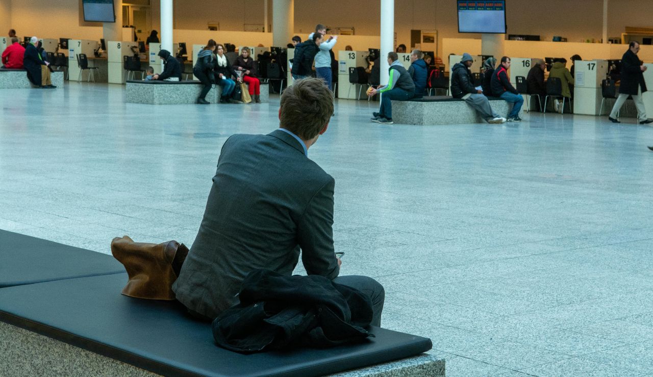 Traveler sitting on luggage looking stressed in a busy airport terminal