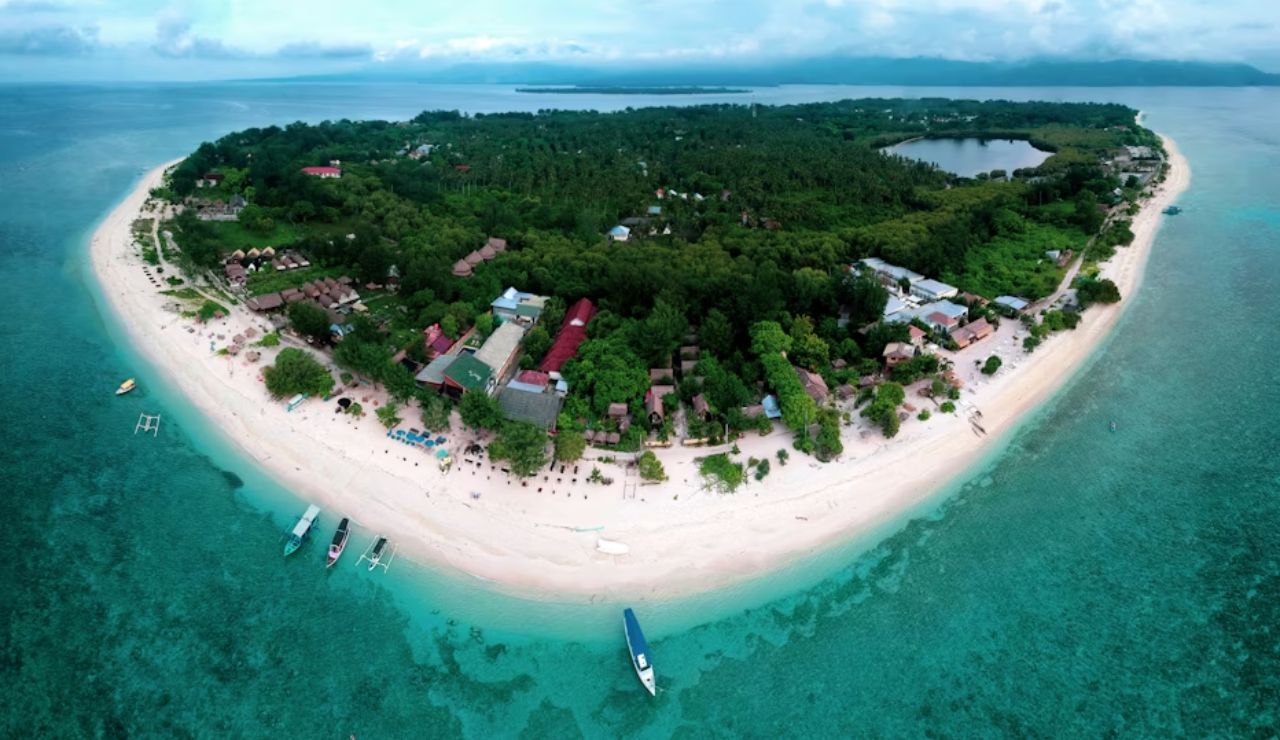 Aerial view of a tropical island with white sandy beaches, turquoise waters, boats along the shore, and lush green vegetation.