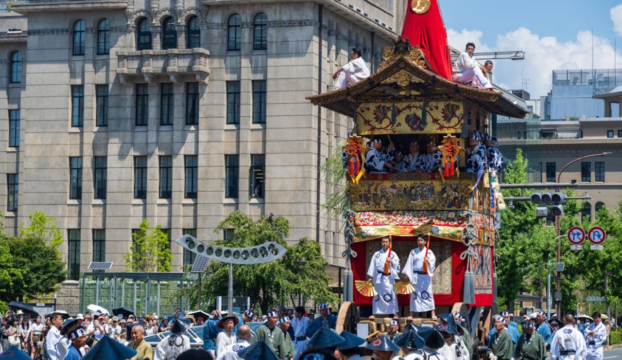 Traditional Japanese float decorated with ornaments and musicians is paraded through city streets during a cultural festival, with crowds watching.