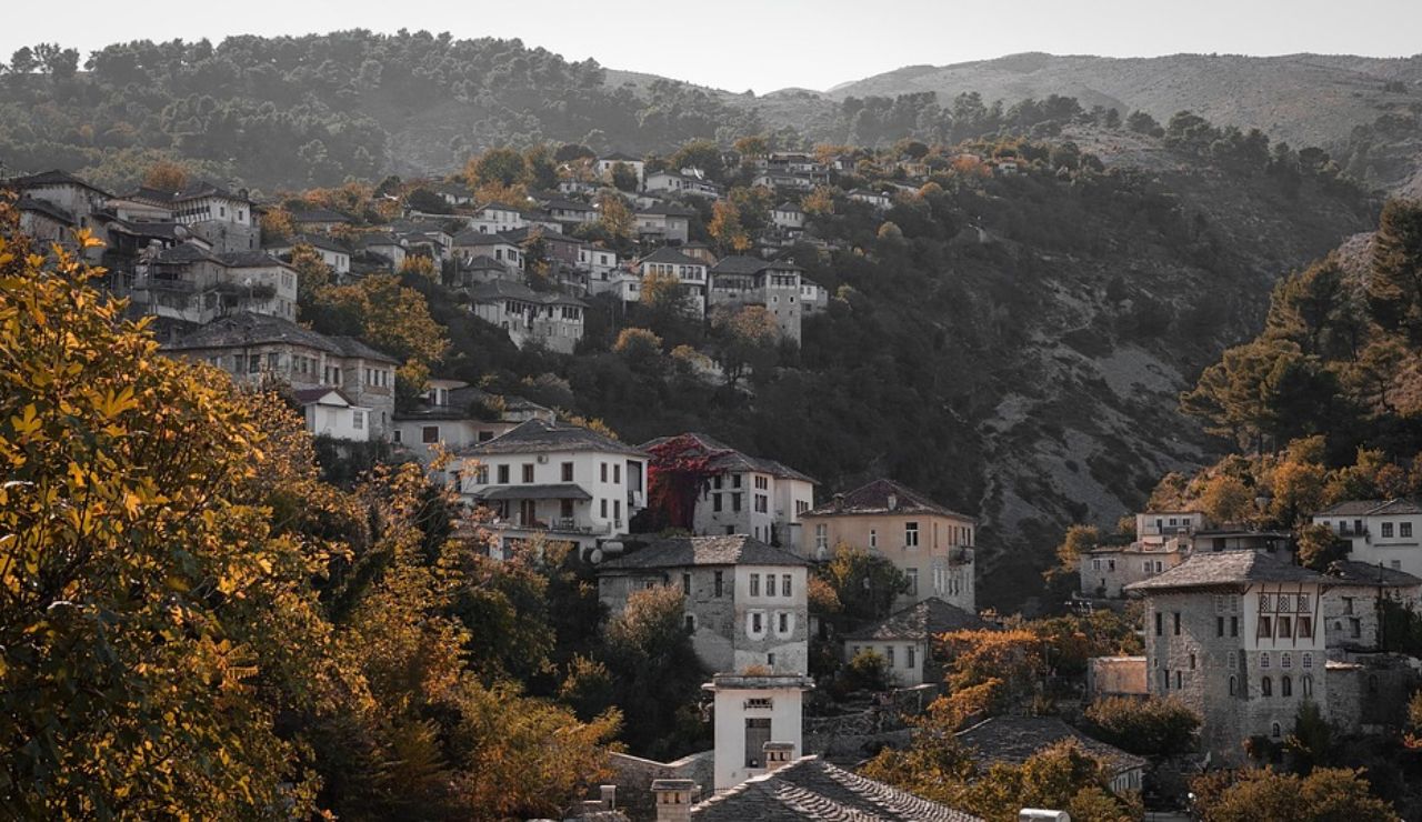 Traditional hillside village with stone houses and red-tiled roofs nestled among autumn trees and forested mountains.