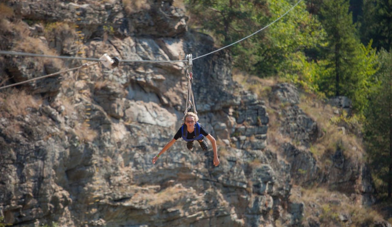 Person ziplining in a superhero position across a rocky canyon with forested cliffs.