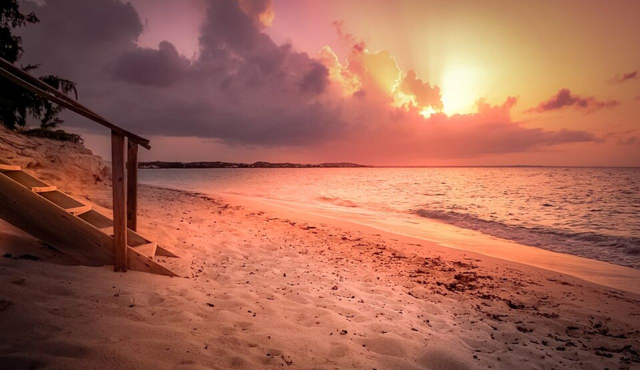 Sunset over Grace Bay in Turks and Caicos, with soft pink and orange light reflecting on the sandy beach and calm waves.