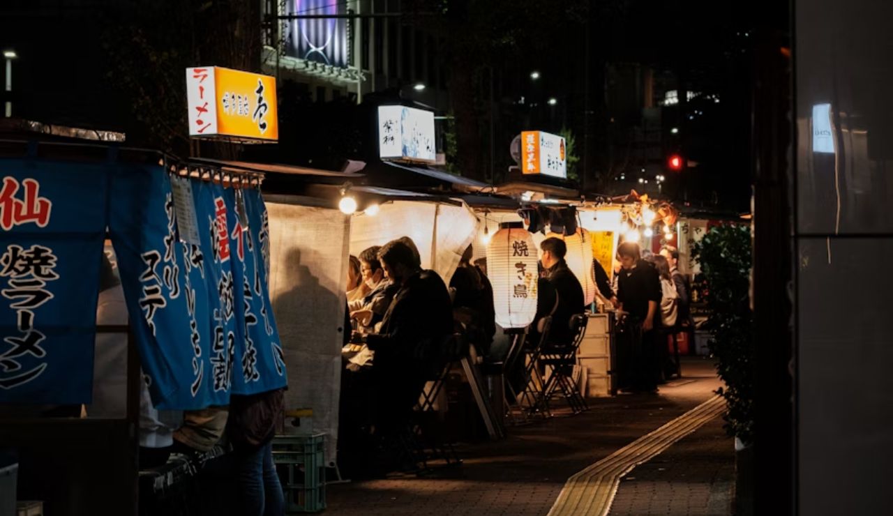 Nighttime view of a Japanese street food market with stalls offering ramen and grilled dishes.