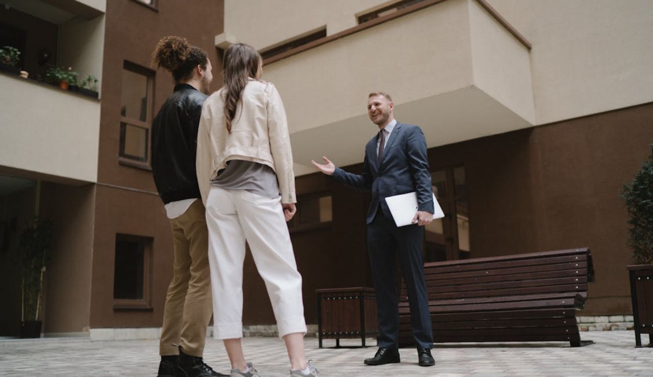 Real estate agent speaking with a couple outside an apartment building, representing housing market challenges in the Pacific Northwest.