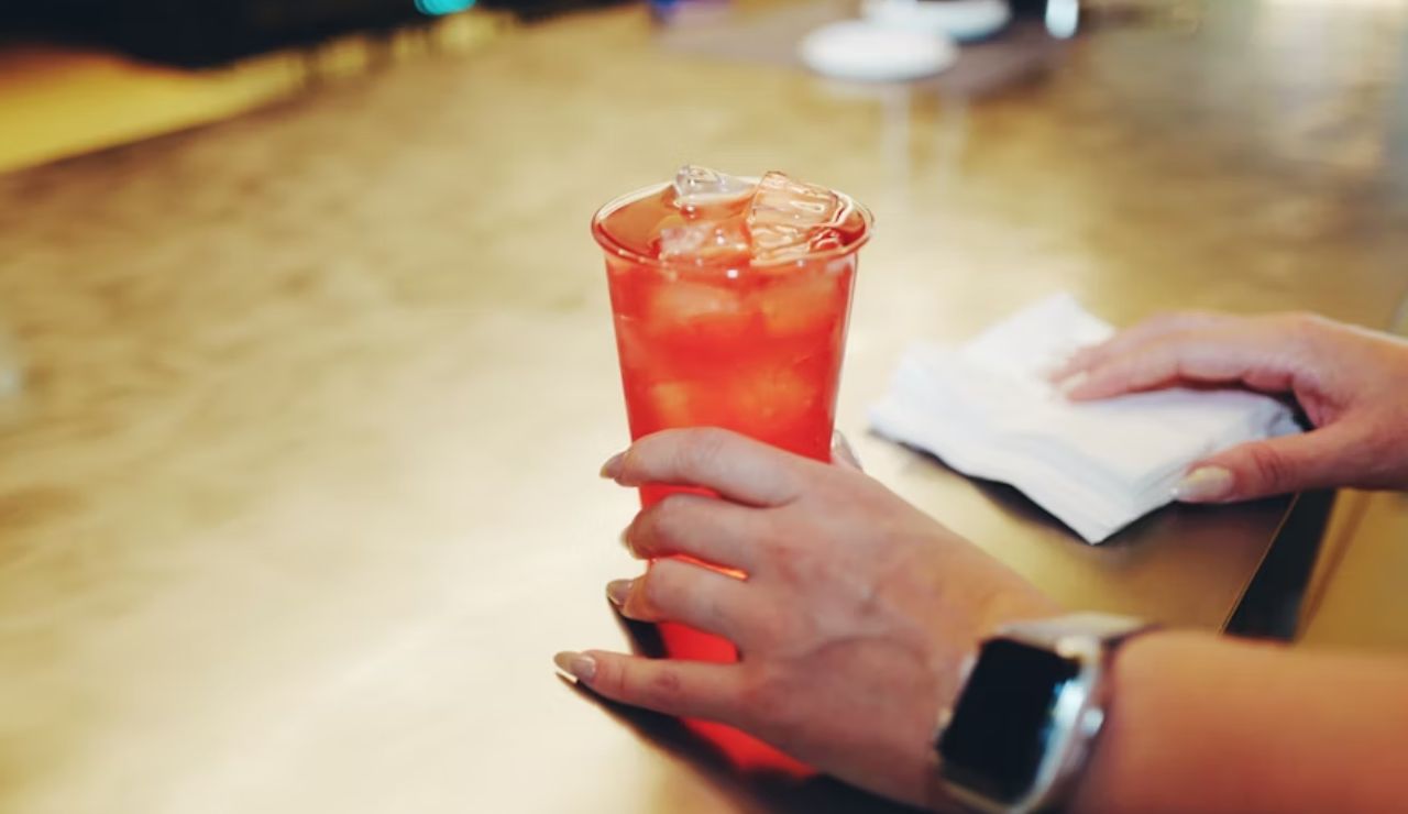 A hand holding a glass of iced drink on a table, with a napkin nearby.