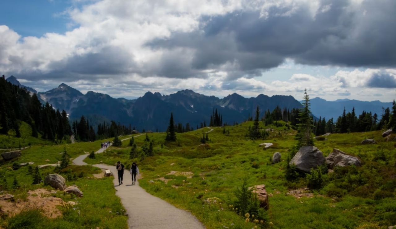 Visitors walking a scenic trail in the Pacific Northwest, surrounded by lush greenery and mountain peaks, showcasing sustainable nature tourism.