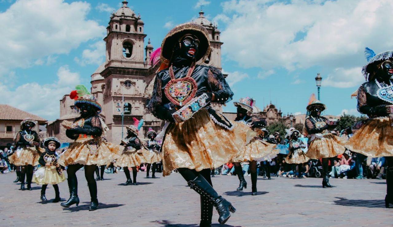 A person in traditional costume and face paint participates in a cultural festival, with historic church towers visible in the background under a partly cloudy sky.