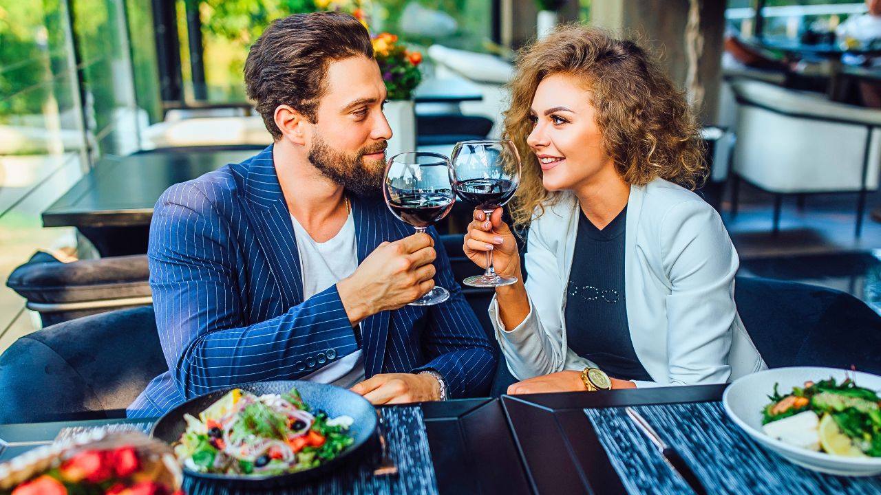 A smiling couple toasts with red wine over a meal at a U.S. restaurant.