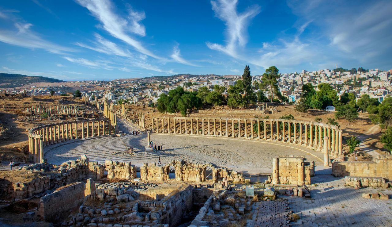 Ancient Roman ruins of Jerash in Jordan, featuring a large oval colonnaded plaza with stone columns and surrounding archaeological remains.