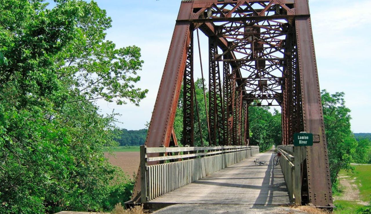 Historic iron truss bridge over the Lamine River on the Katy Trail in Missouri, featuring a wooden path for bikes and pedestrians surrounded by greenery.