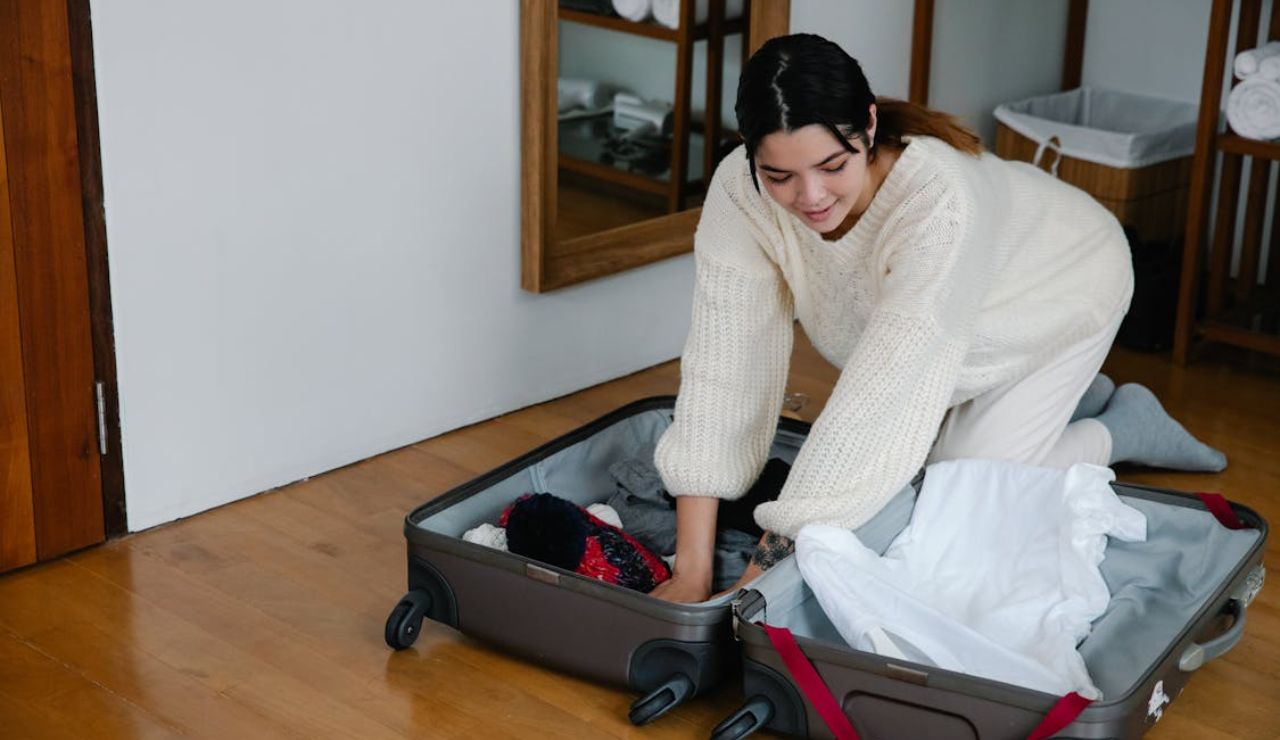 Woman in cozy clothes kneeling on the floor while packing a suitcase.