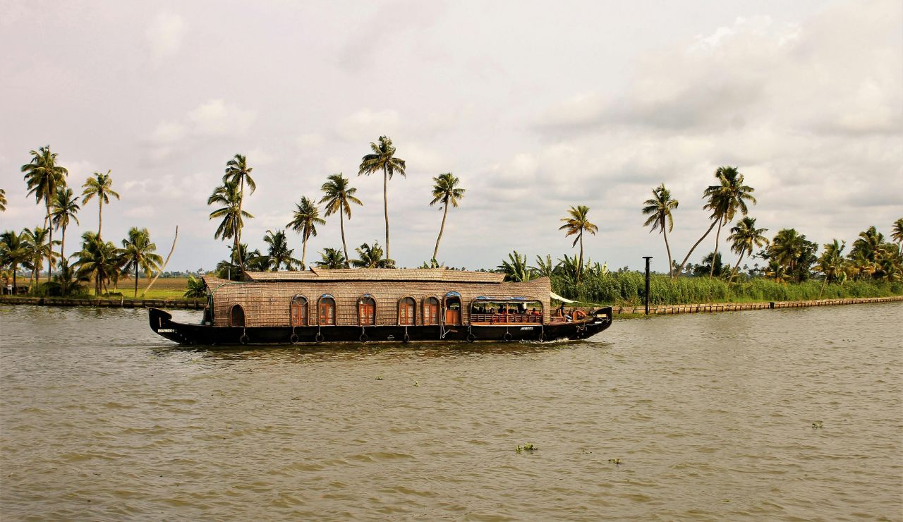 A traditional houseboat gliding along a palm-fringed backwater canal in Kerala.