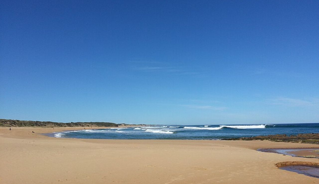 A wide, quiet beach with golden sand, gentle waves, and a clear blue sky—perfect for a peaceful seaside escape.