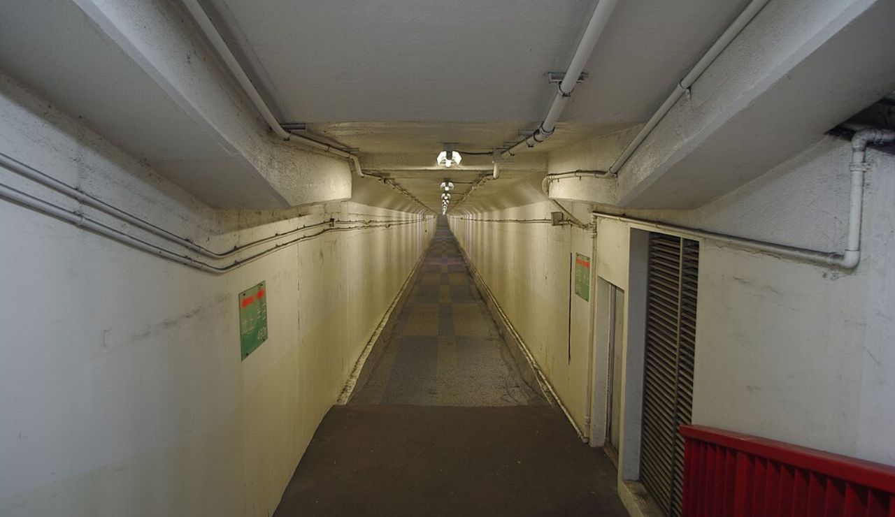Long, narrow underground tunnel with white walls and overhead lighting.