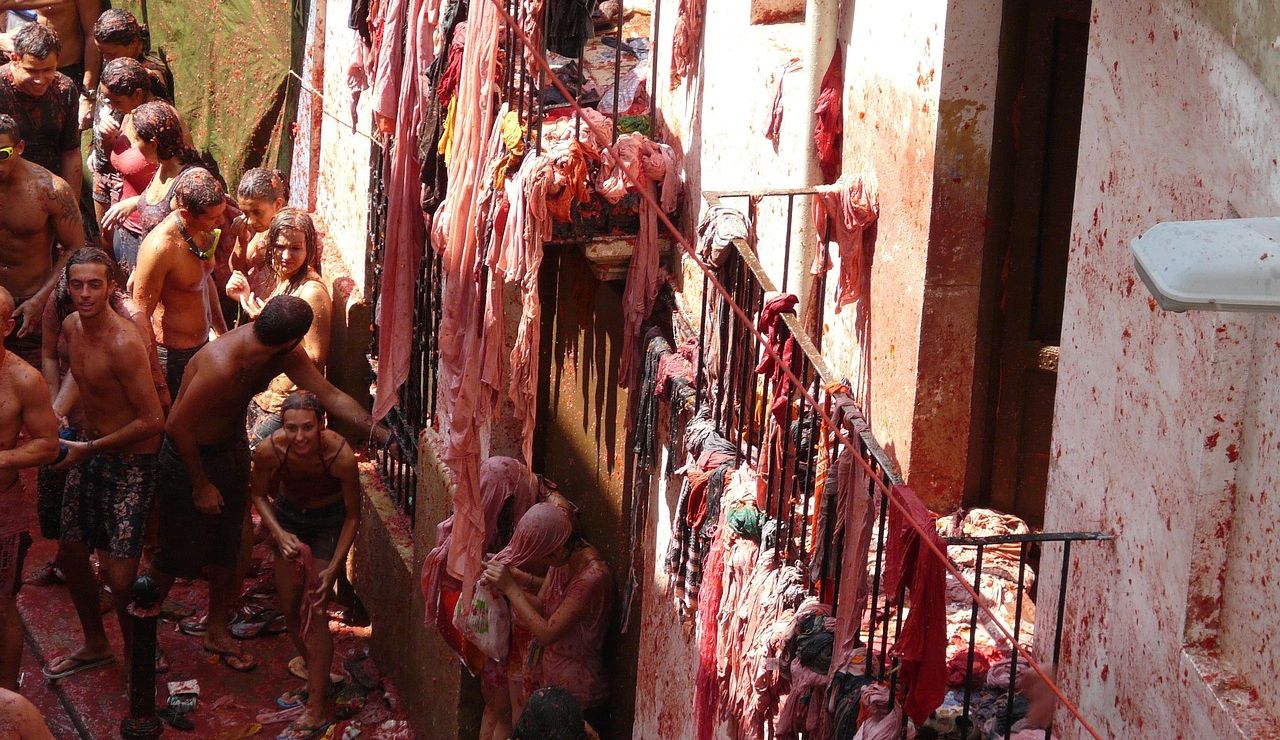 People covered in smashed tomatoes participate in La Tomatina, a messy and vibrant tomato-throwing festival on a narrow, crowded street.