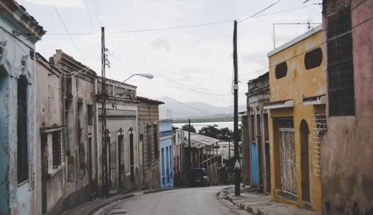 Narrow street lined with old, colorful buildings in a quiet town with mountains visible in the background.