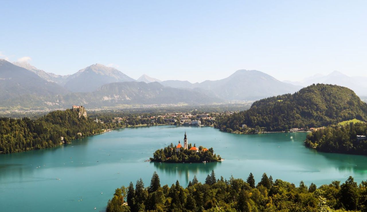 Aerial view of Lake Bled in Slovenia with its island church, surrounded by forested hills and mountains.