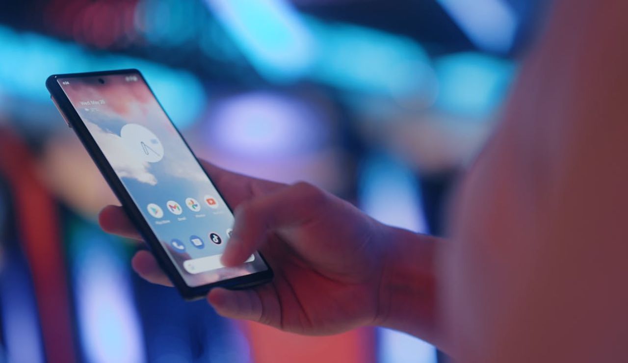 Close-up of a person using a smartphone with a colorful blurred background, showing a home screen with app icons.