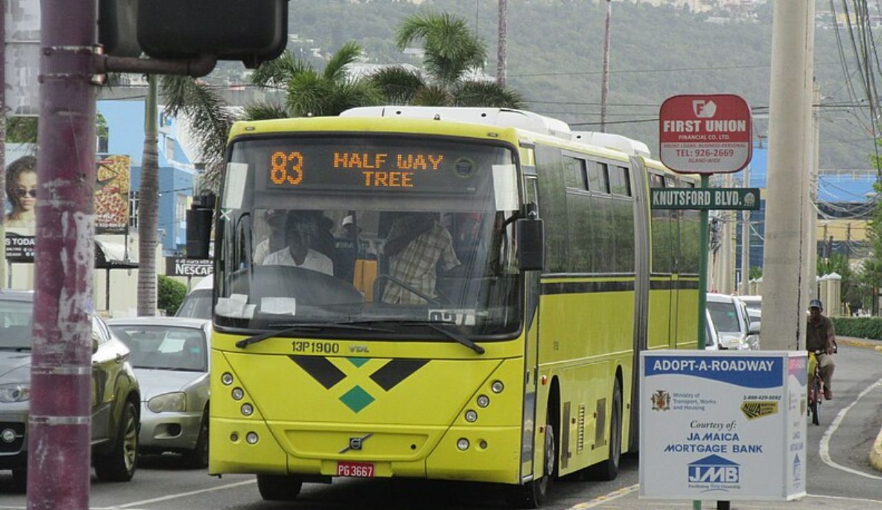 Yellow public bus in Jamaica with route number 83 to Half Way Tree, driving on a busy city street.