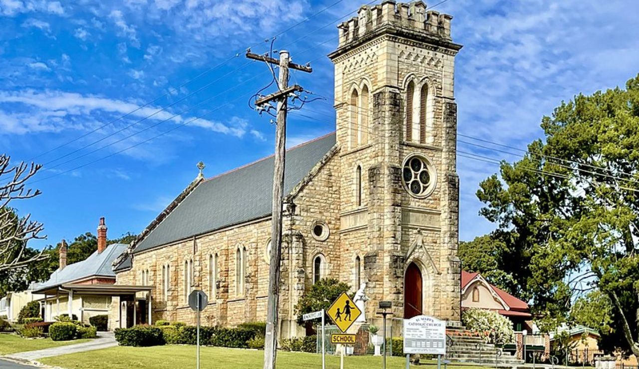 A historic stone church with a tall tower and red door under blue skies.