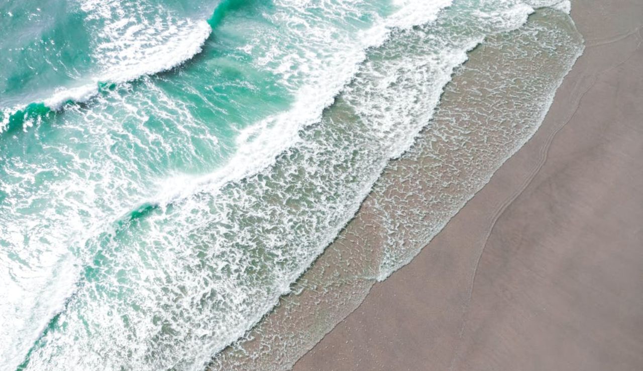 Aerial view of turquoise waves crashing onto a smooth sandy beach.
