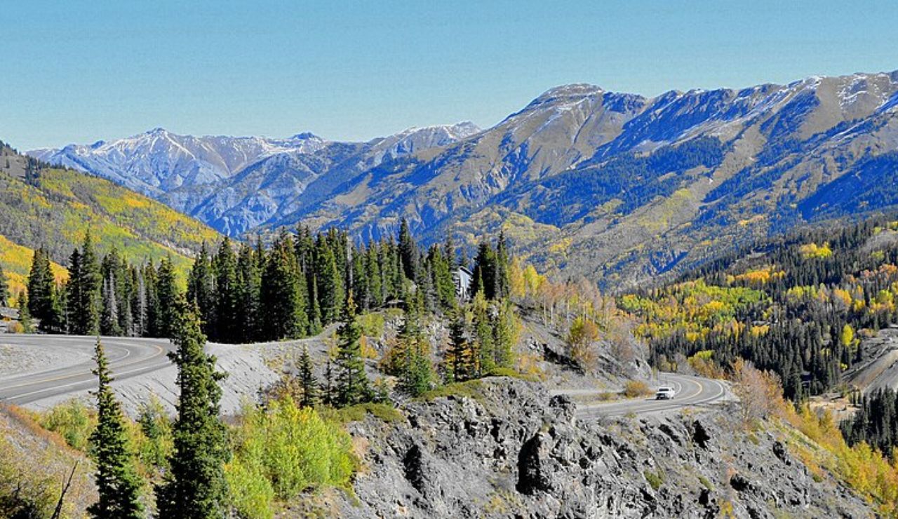 Million Dollar Highway winding through colorful autumn trees and rugged Colorado mountains.