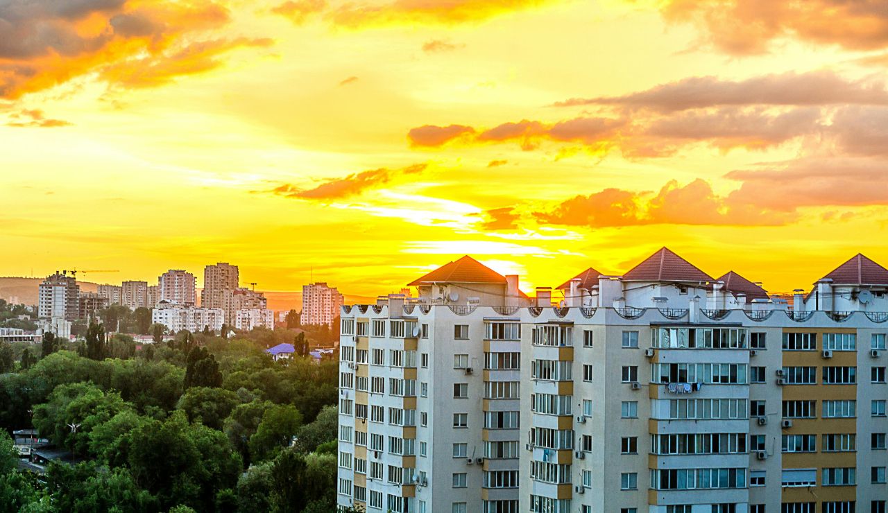 Sunset casting a golden glow over a residential apartment complex with a cityscape and green trees in the background.