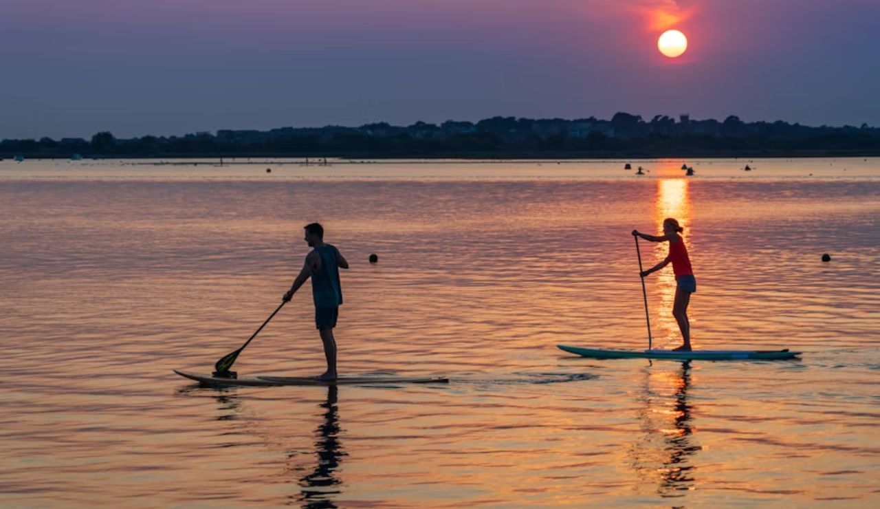 A couple enjoys paddleboarding at sunset, gliding over calm golden waters.