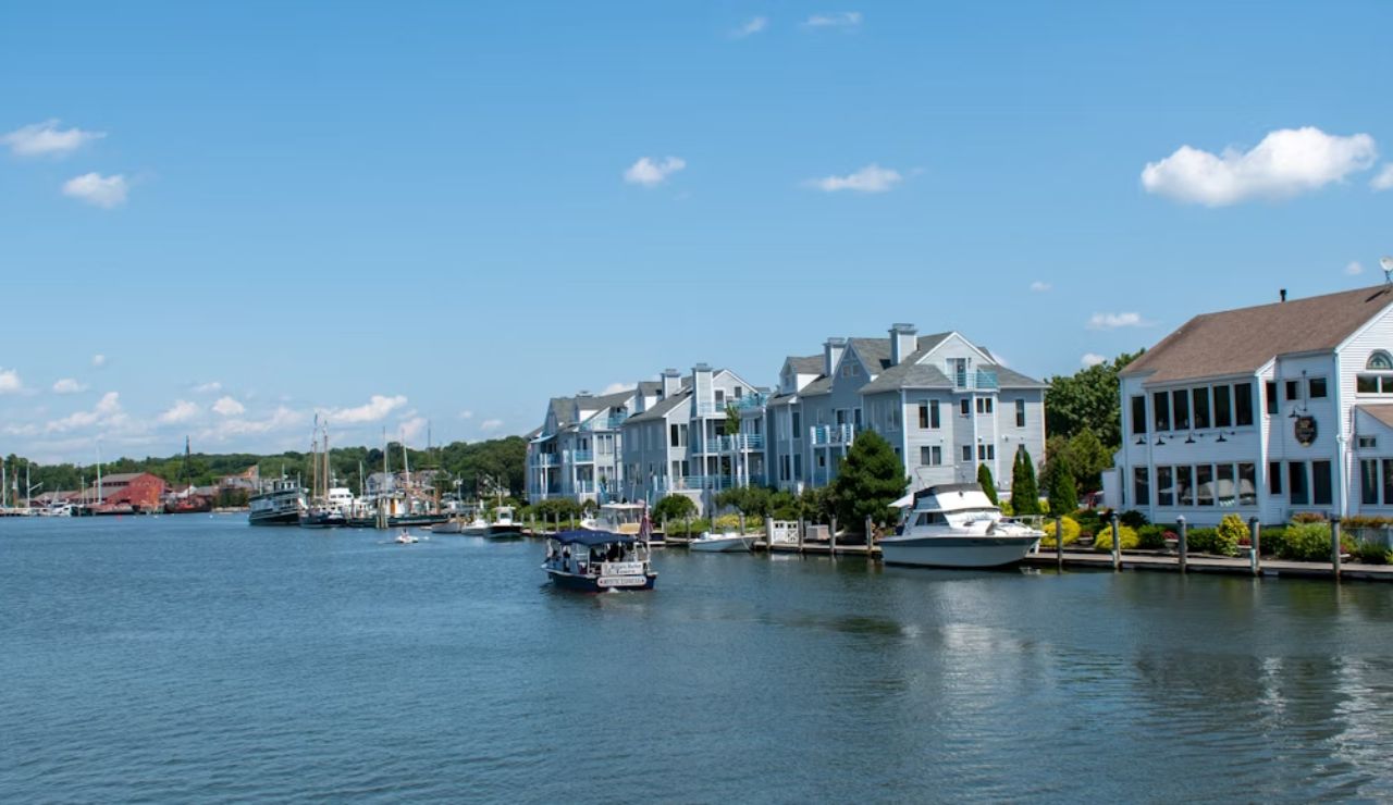 Waterfront homes and boats lined along a calm river under a clear blue sky.