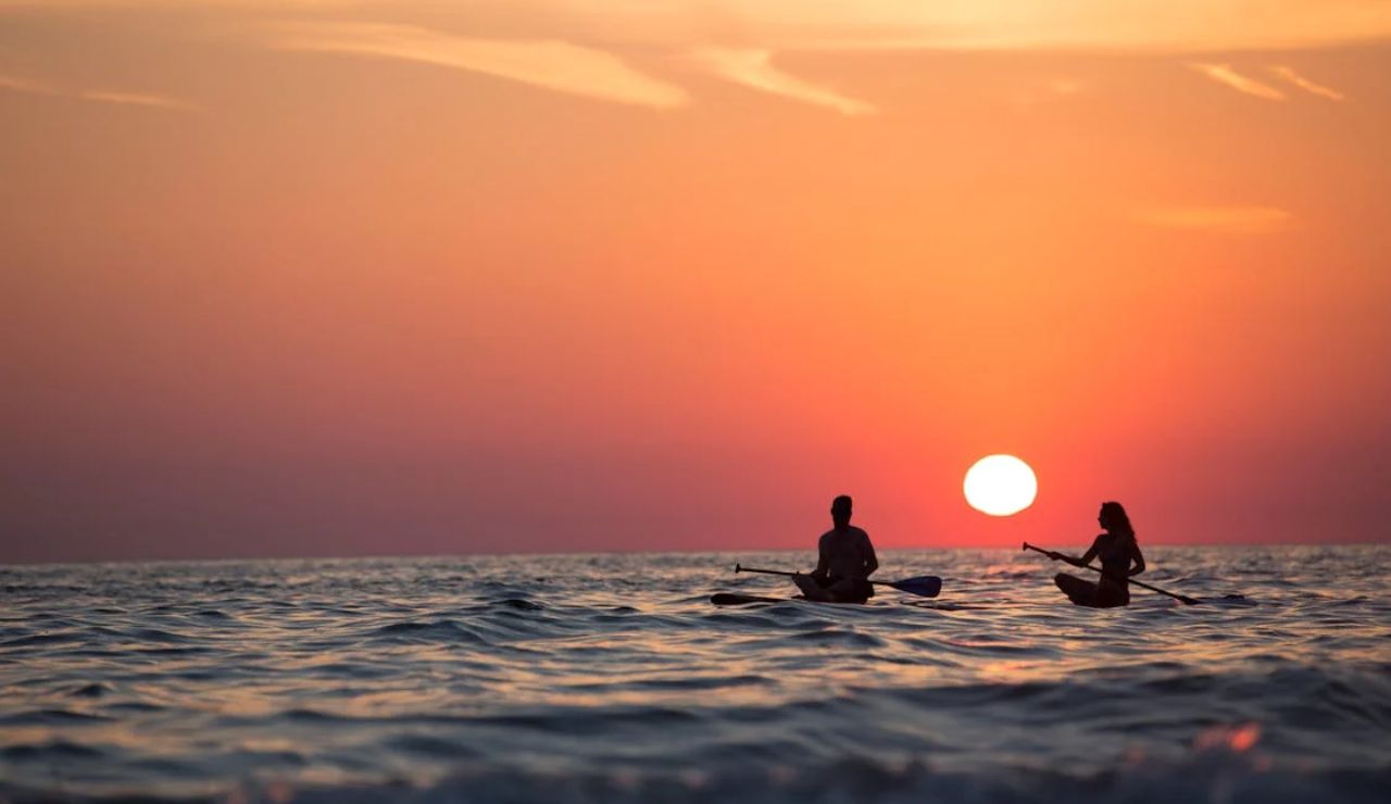 Two kayakers paddle across the gentle waves off Namotu Island, Fiji, under a breathtaking sunset sky.