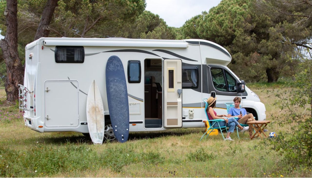 Couple relaxing outside RV with surfboards, enjoying nature as their backyard.