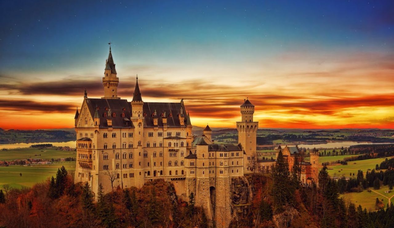 Neuschwanstein Castle in Germany at sunset with a dramatic sky and forested landscape.
