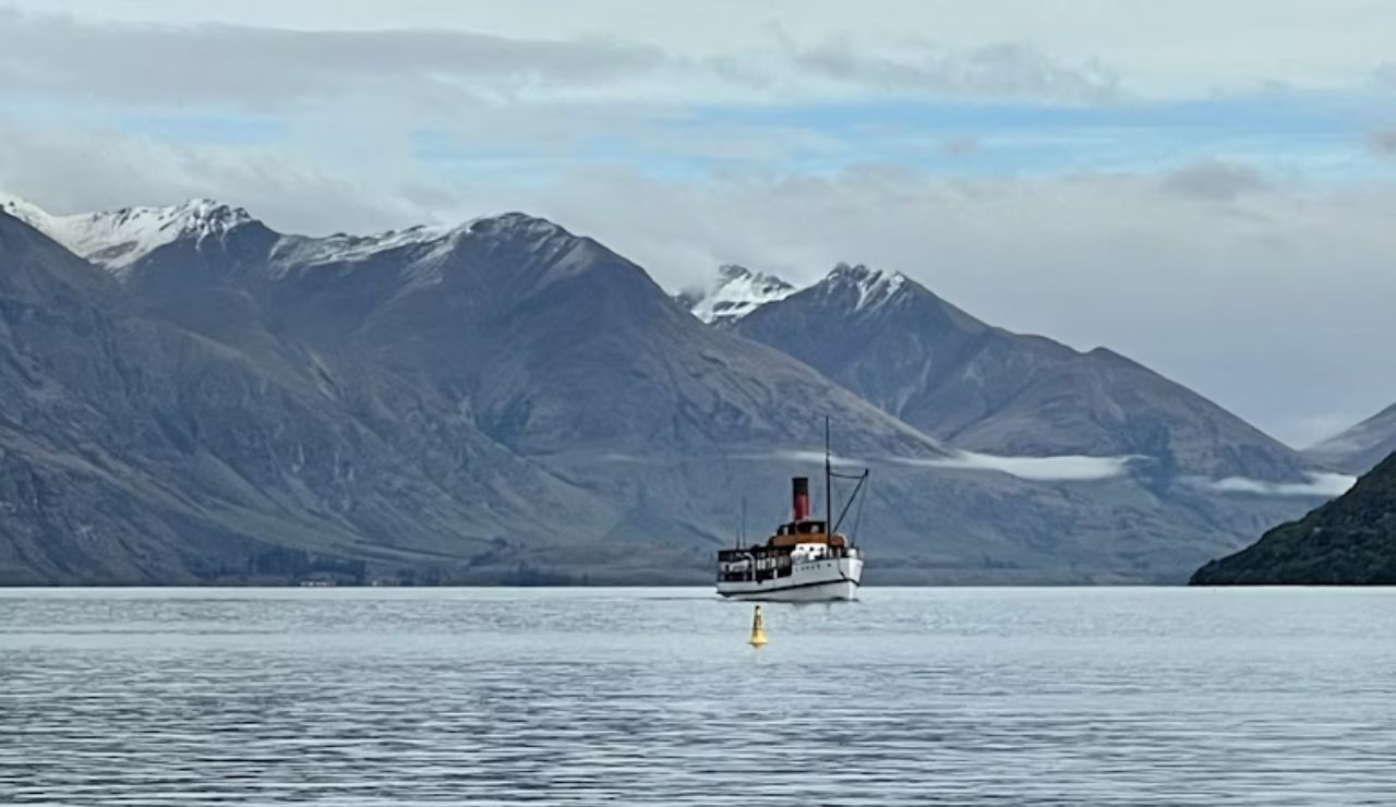 Vintage steamship sailing on a calm lake with snow-capped mountains behind.