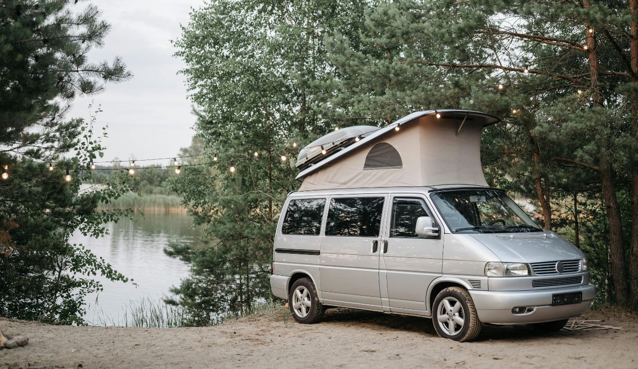 A campervan parked beside a lake with mountains in the background at sunset.