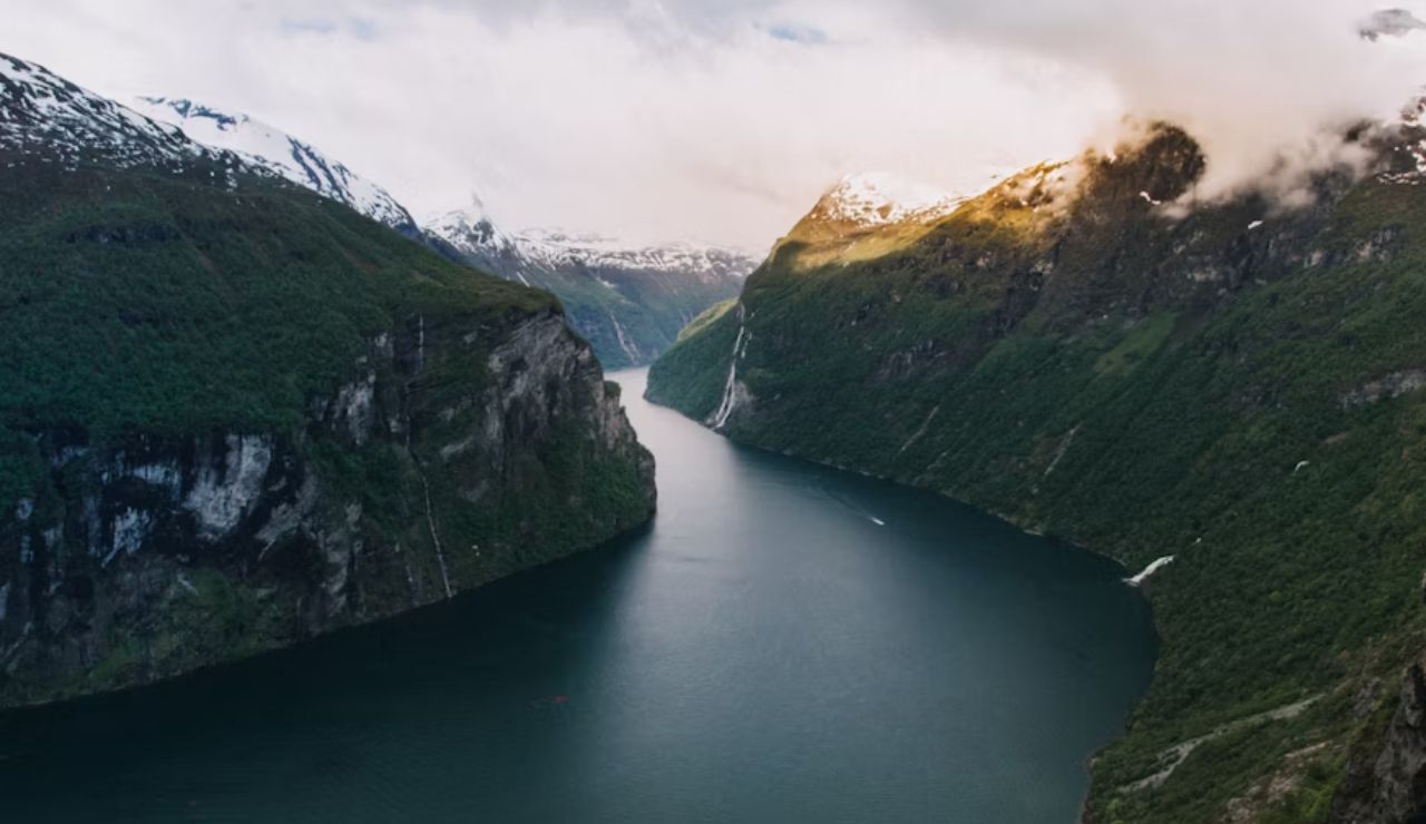 A scenic fjord winding between steep, green cliffs and snow-capped peaks.
