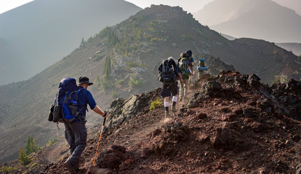 Group of hikers with backpacks trekking along a rugged mountain trail under hazy skies.