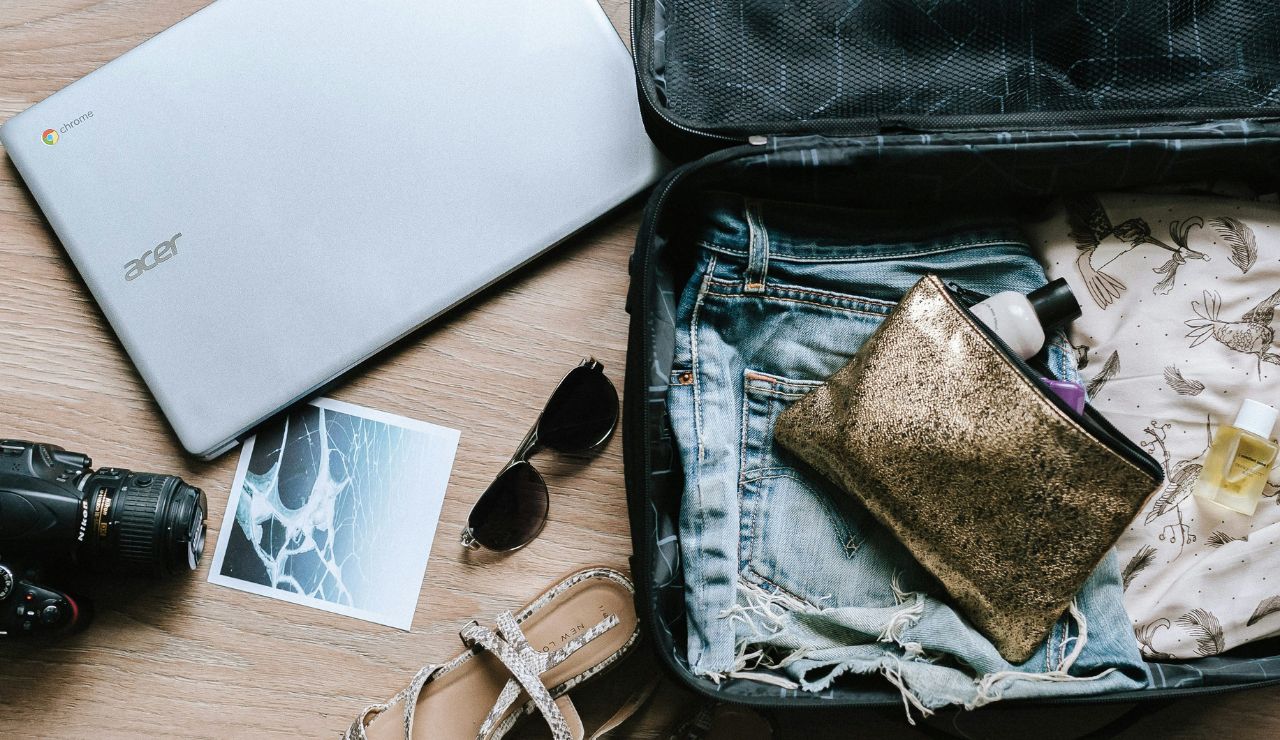 Open suitcase with clothes and travel essentials next to a laptop and camera.