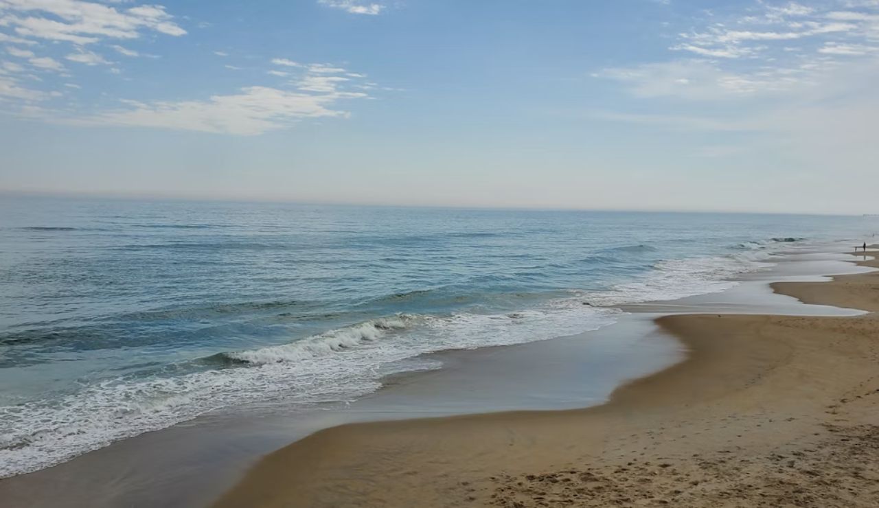 Peaceful beach with gentle waves and a mostly empty shoreline under a partly cloudy sky.