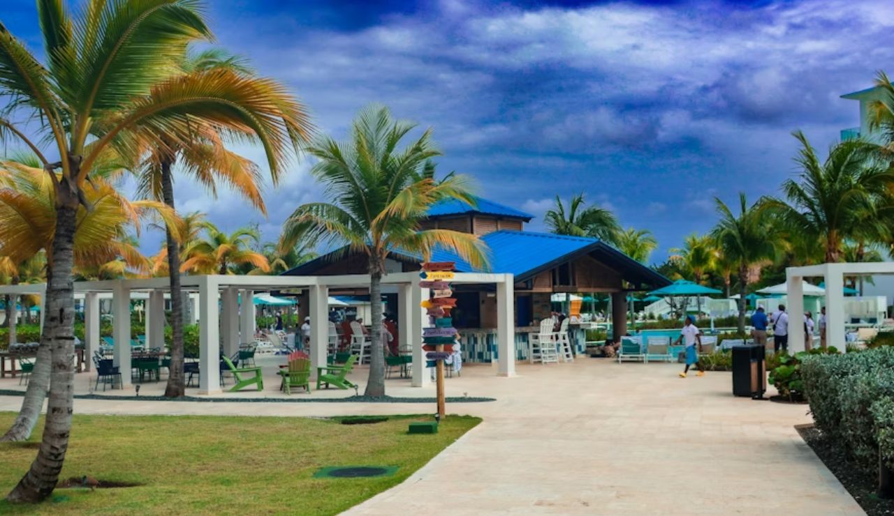 Tropical resort area with palm trees, outdoor seating, and colorful buildings under a dramatic cloudy sky.