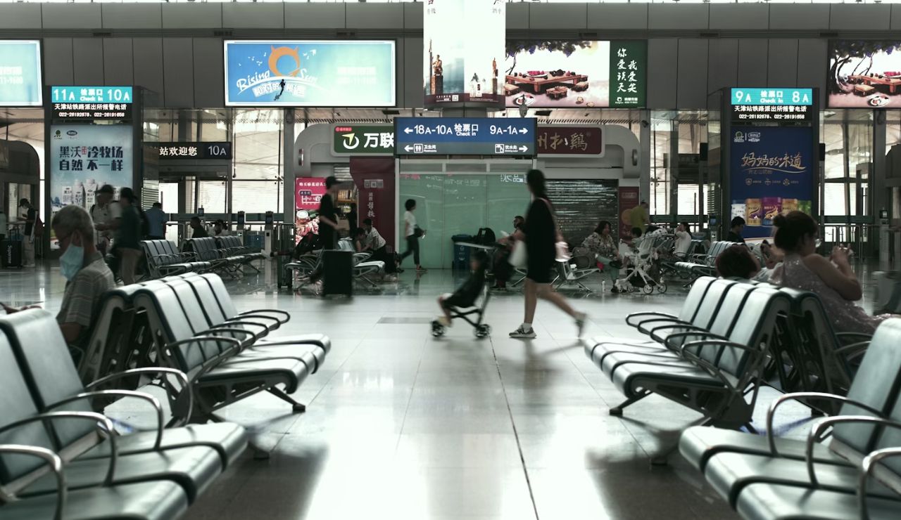 People waiting and walking through a spacious airport terminal with seating and signs.