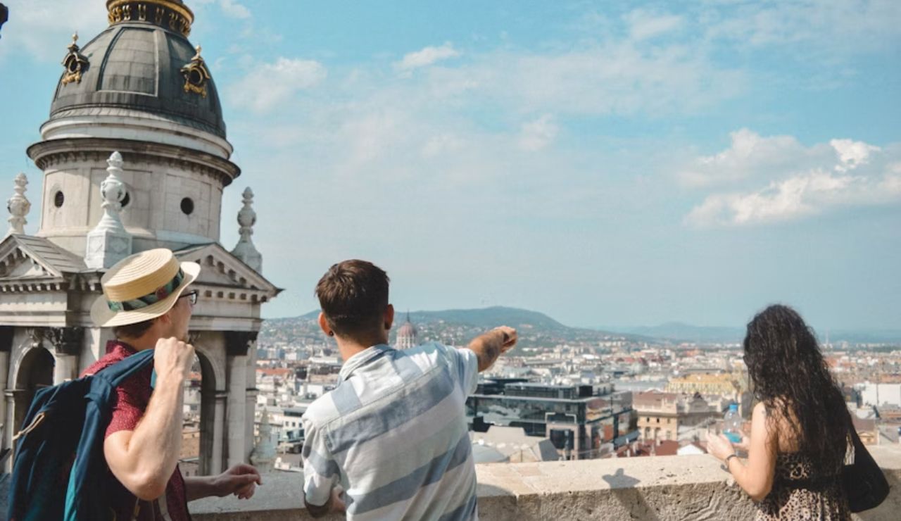 A group of three people, one pointing towards the city skyline while the others look on, enjoying the view from a rooftop.