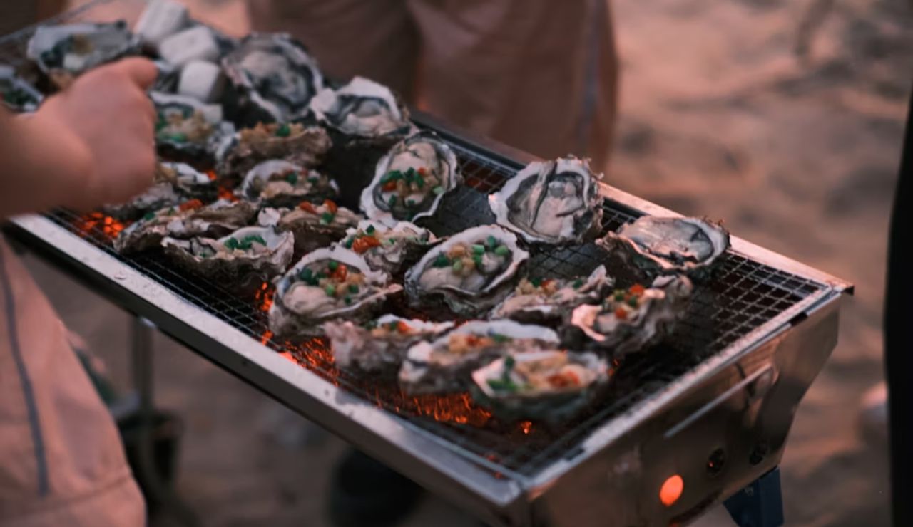 Grilled Puget Sound oysters topped with vegetables over open flame.