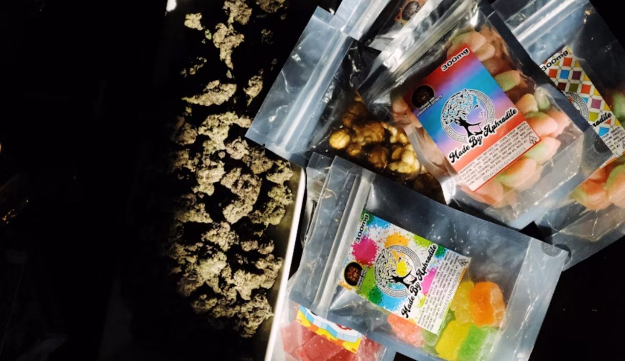 Assorted cannabis edibles and snacks in resealable bags next to dried cannabis buds on a tray.
