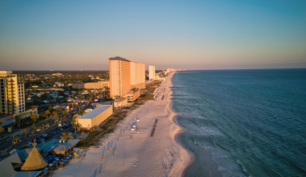 Aerial view of a coastal city with high-rise buildings lining a long stretch of sandy beach at sunset.