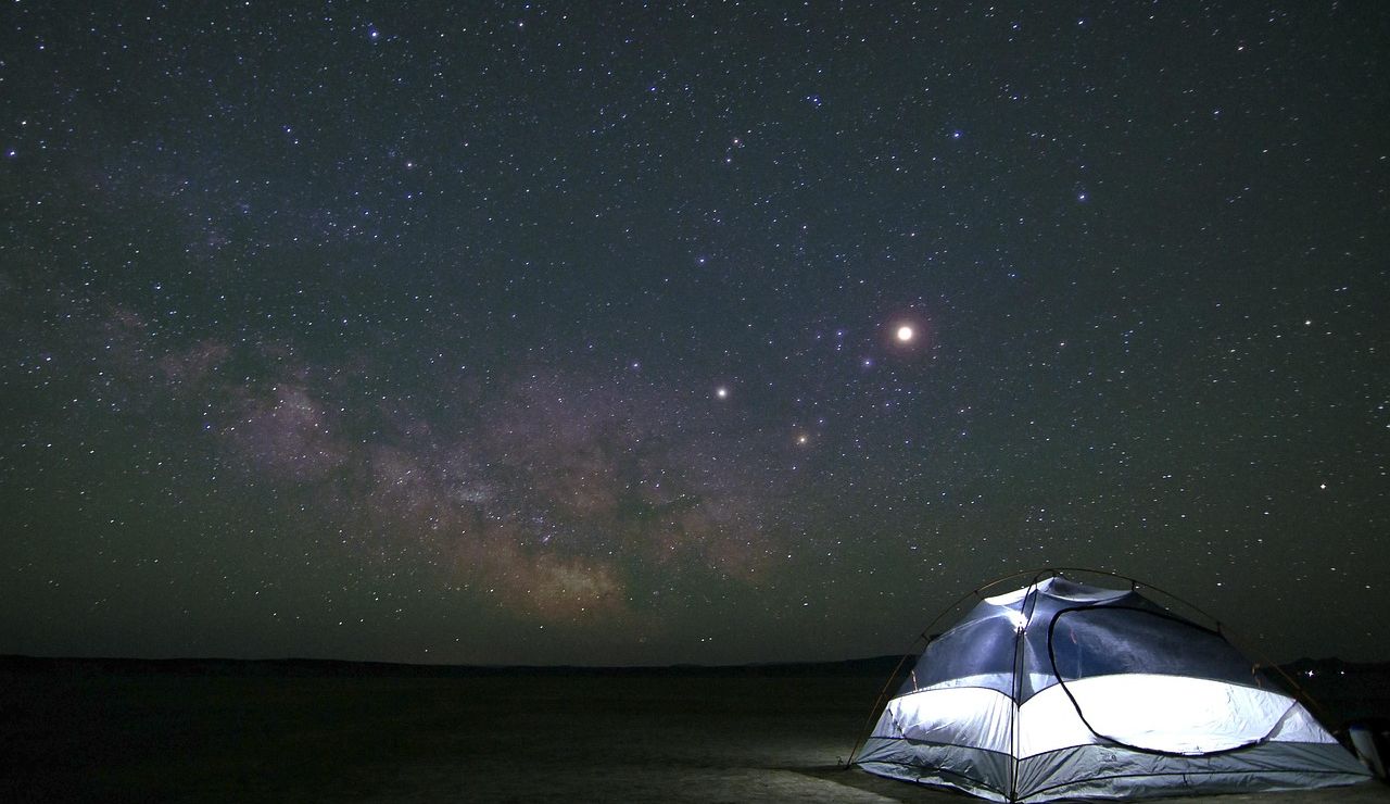 A glowing tent sits under a star-filled sky and Milky Way.