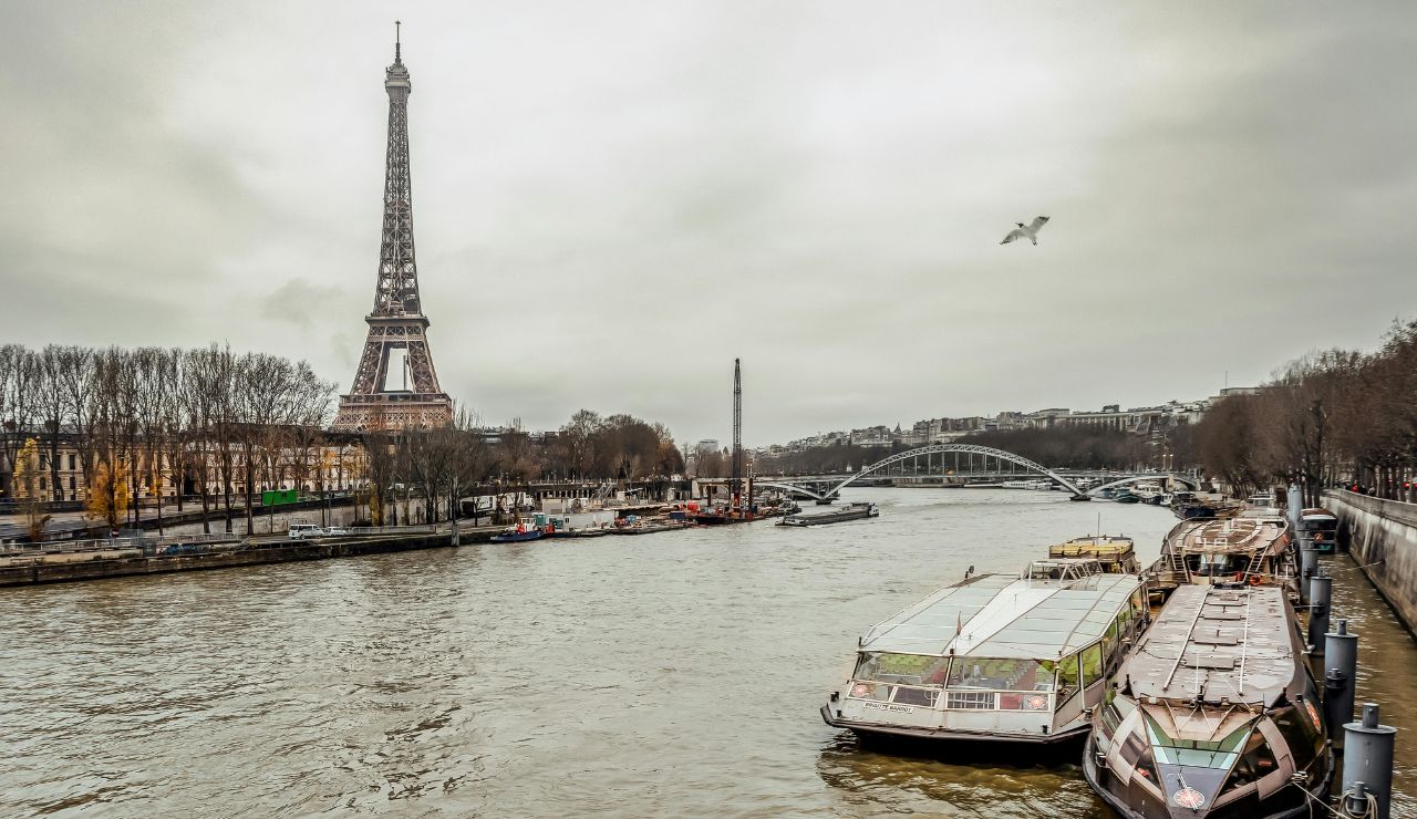  View of the Eiffel Tower and the Seine River in Paris with boats docked along the riverbank on a cloudy day.