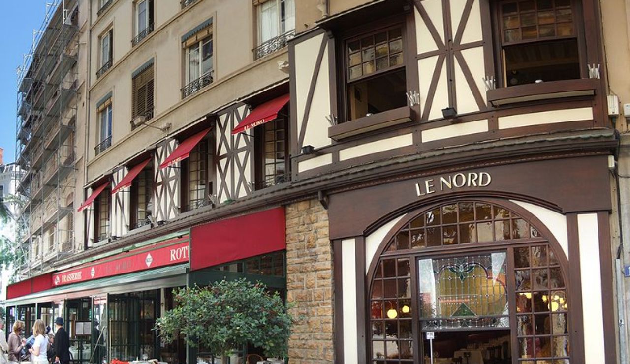 Exterior of the traditional French restaurant "Le Nord" with Tudor-style architecture, red awnings, and a large stained glass window.