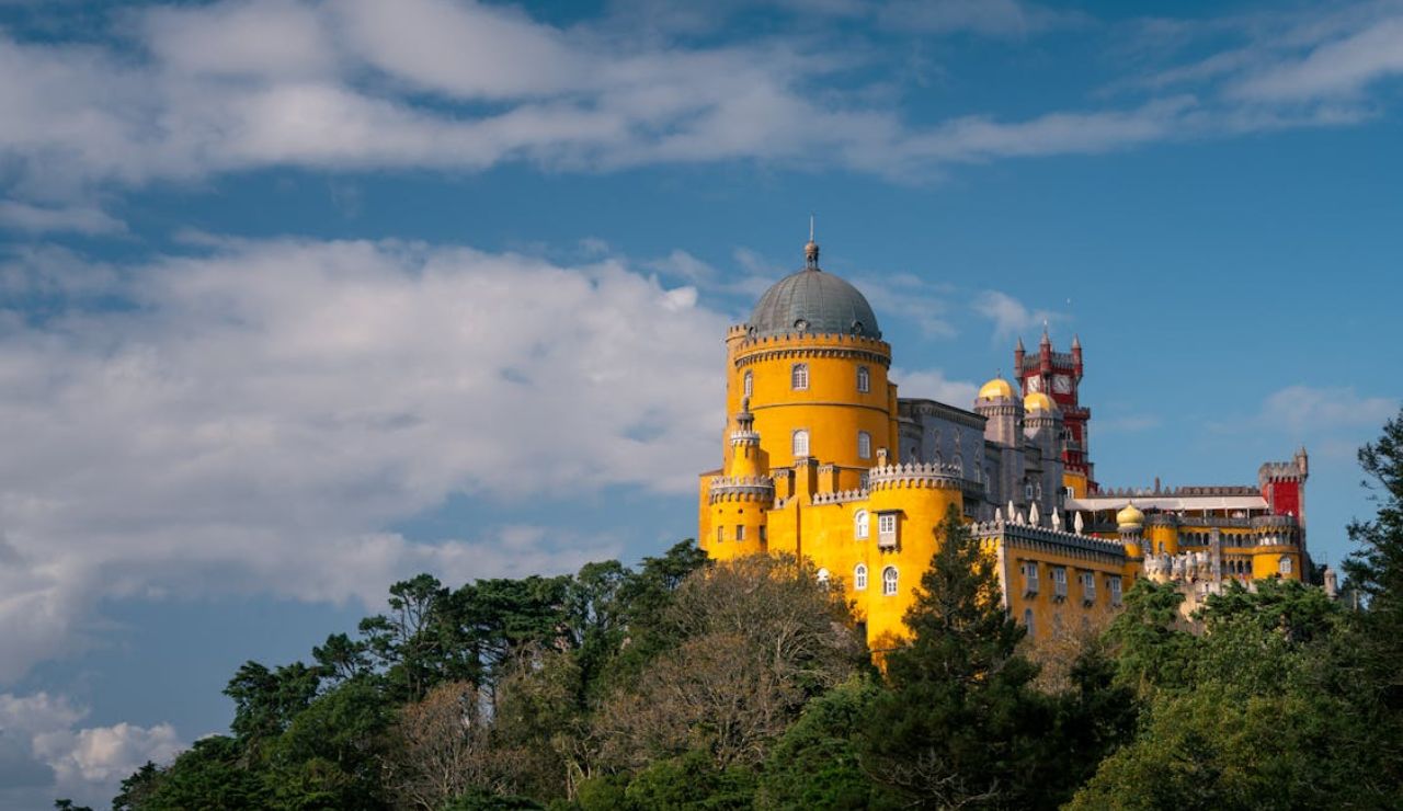 Bright yellow and red Pena Palace in Sintra, Portugal, standing on a forested hill under a blue sky with clouds.