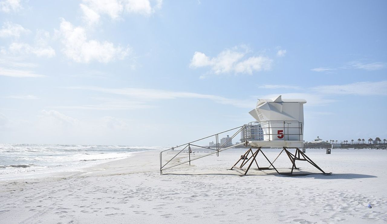Empty beach with white sand and a lifeguard tower marked with the number 5 overlooking the ocean on a bright, sunny day.