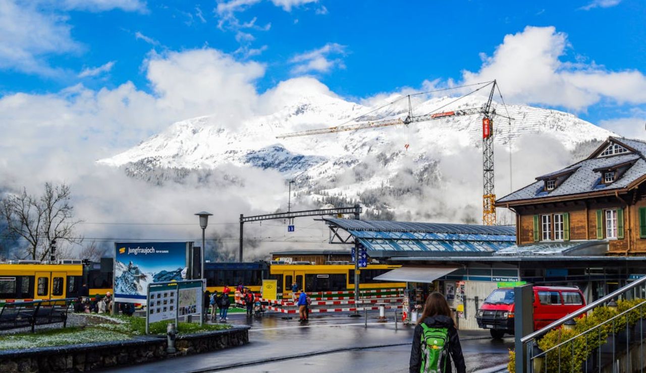 Train station with snow-capped mountains in the background, a traveler walking with a suitcase.